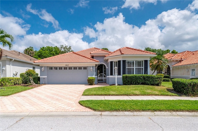 mediterranean / spanish-style house featuring decorative driveway, a tile roof, stucco siding, a garage, and a front lawn