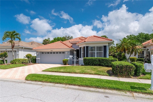 mediterranean / spanish house featuring decorative driveway, stucco siding, a front yard, a garage, and a tiled roof