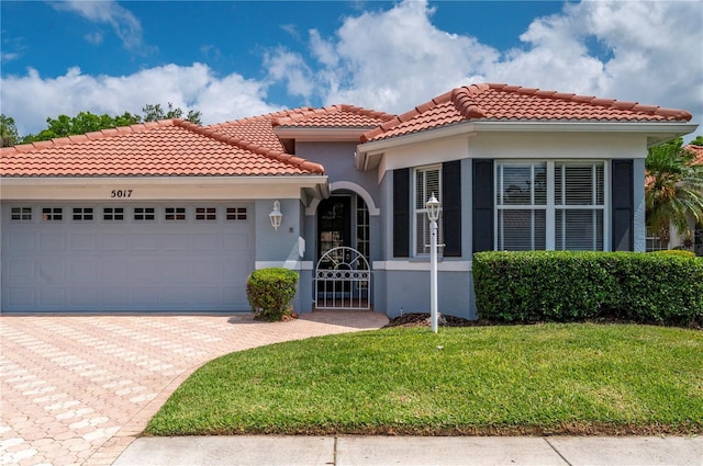 mediterranean / spanish house with a garage, a tiled roof, decorative driveway, stucco siding, and a front yard