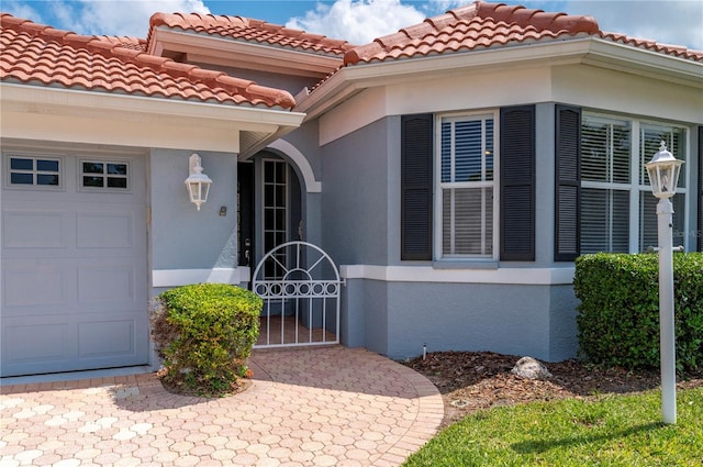 doorway to property with an attached garage, a gate, and stucco siding