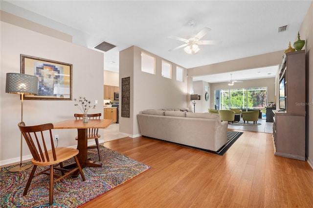 living room with light wood finished floors, a ceiling fan, visible vents, and baseboards