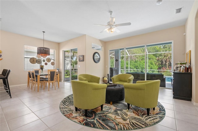 living area with ceiling fan with notable chandelier, a wealth of natural light, visible vents, and light tile patterned floors