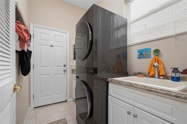 clothes washing area featuring light tile patterned floors, cabinet space, a sink, and stacked washer and clothes dryer