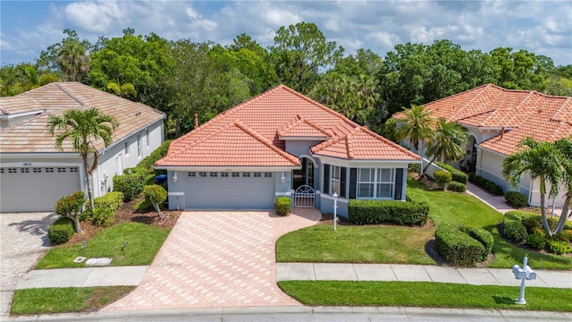 mediterranean / spanish house featuring a garage, a tiled roof, decorative driveway, stucco siding, and a front lawn