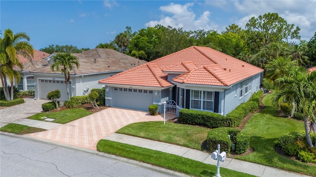 mediterranean / spanish-style house with a garage, a tiled roof, decorative driveway, a front lawn, and stucco siding