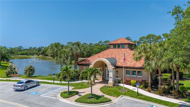 view of front of house with a tiled roof, a water view, french doors, uncovered parking, and stucco siding