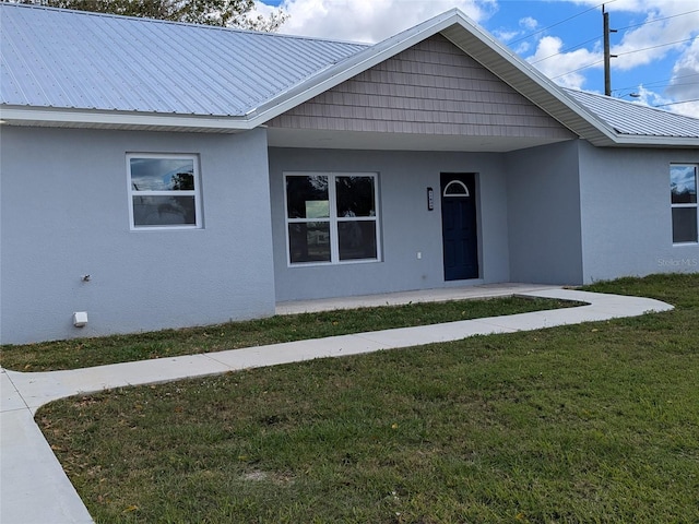 view of front facade with metal roof, a front lawn, and stucco siding