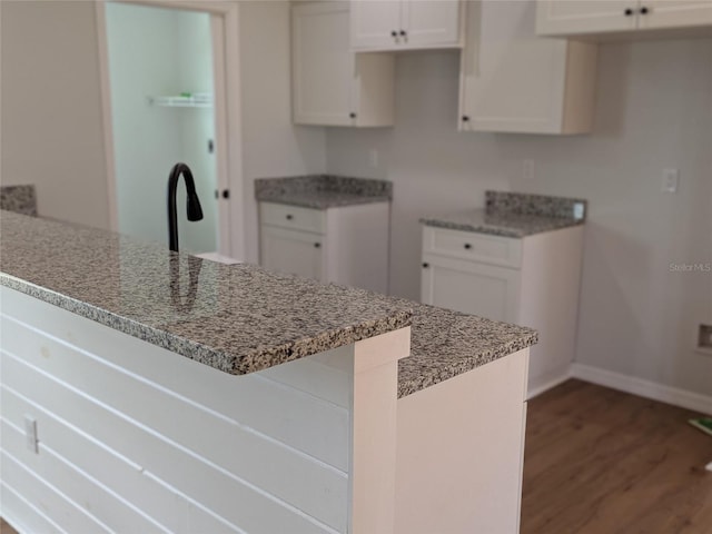 kitchen with light stone countertops, baseboards, dark wood-style floors, and white cabinets