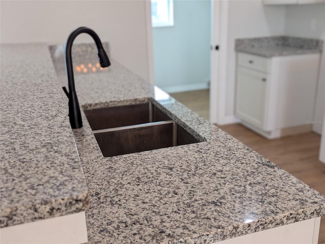 interior details with wood finished floors, white cabinetry, a sink, and light stone countertops