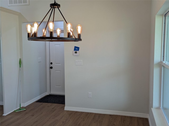 foyer entrance with baseboards, wood finished floors, visible vents, and an inviting chandelier