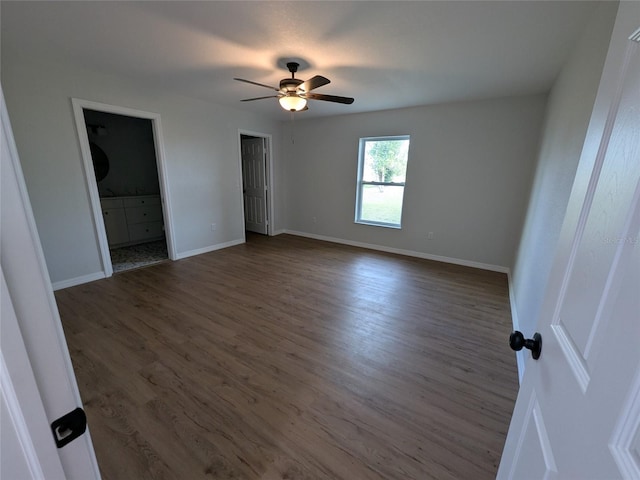 unfurnished bedroom featuring ensuite bathroom, dark wood finished floors, a ceiling fan, and baseboards