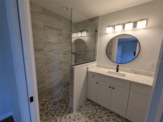 full bathroom featuring a textured wall, a walk in shower, and vanity