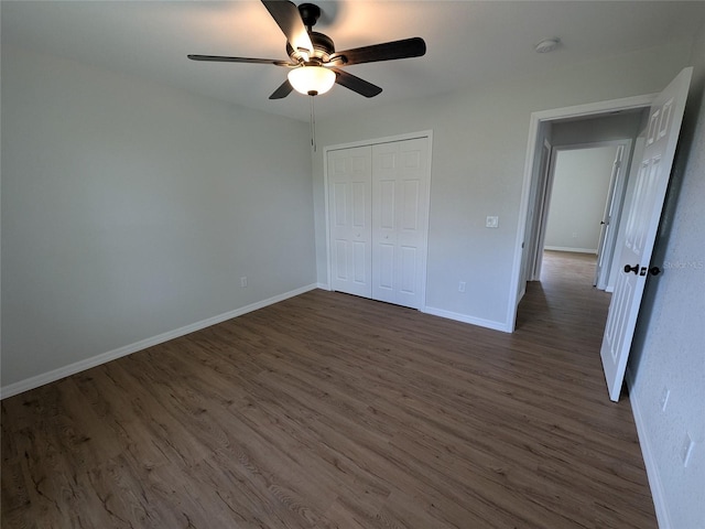 unfurnished bedroom with dark wood-style floors, a closet, ceiling fan, and baseboards