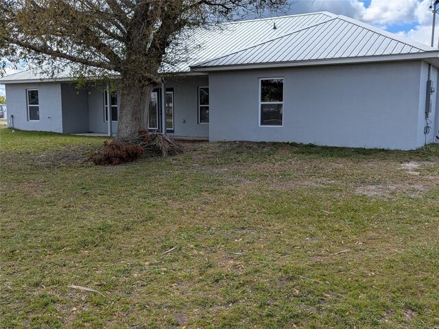 back of house featuring metal roof, a lawn, and stucco siding