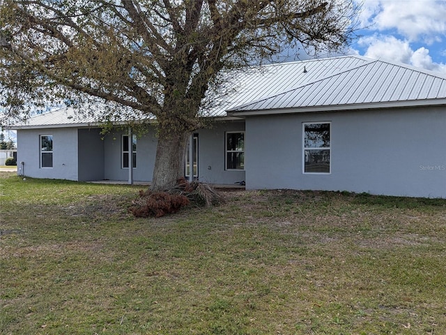 rear view of house with metal roof, a lawn, and stucco siding