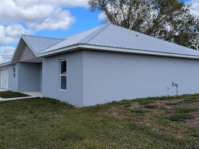 view of property exterior with a garage, metal roof, a lawn, and stucco siding