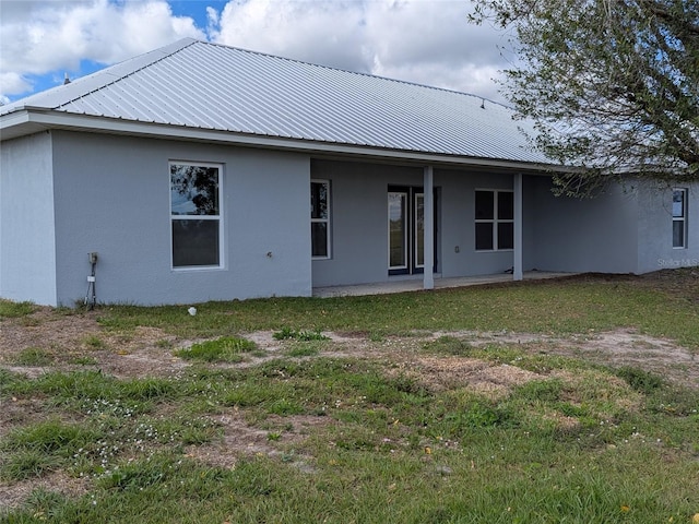 rear view of property featuring a yard, a patio area, metal roof, and stucco siding