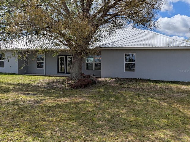 rear view of house with metal roof, a lawn, and stucco siding