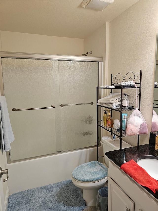full bath with enclosed tub / shower combo, toilet, vanity, and a textured wall