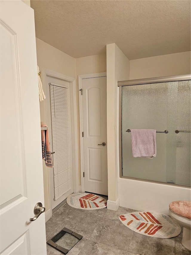 bathroom featuring toilet, combined bath / shower with glass door, a closet, and a textured ceiling