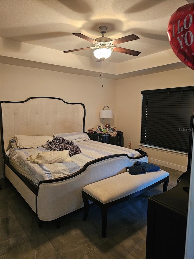 bedroom with a raised ceiling, a ceiling fan, and baseboards