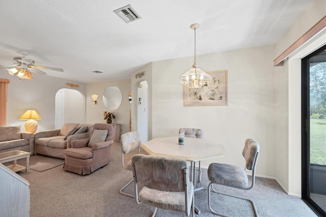 carpeted dining area featuring ceiling fan with notable chandelier, visible vents, arched walkways, and baseboards