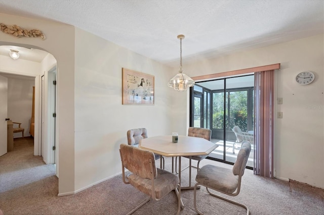 carpeted dining room featuring baseboards, arched walkways, a textured ceiling, and an inviting chandelier