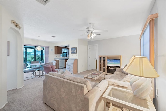 living room featuring light carpet, visible vents, and ceiling fan with notable chandelier