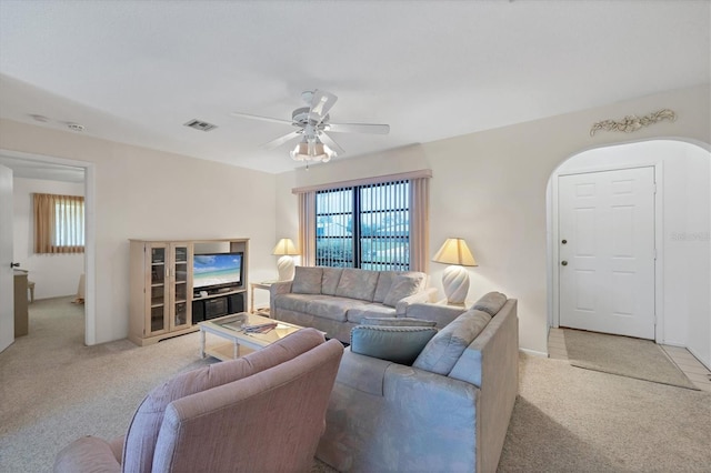 living area with arched walkways, visible vents, light colored carpet, and a ceiling fan