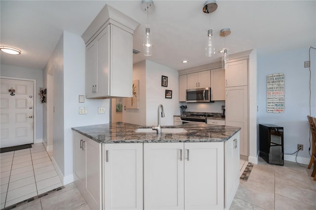 kitchen featuring light tile patterned floors, dark stone counters, appliances with stainless steel finishes, a peninsula, and a sink