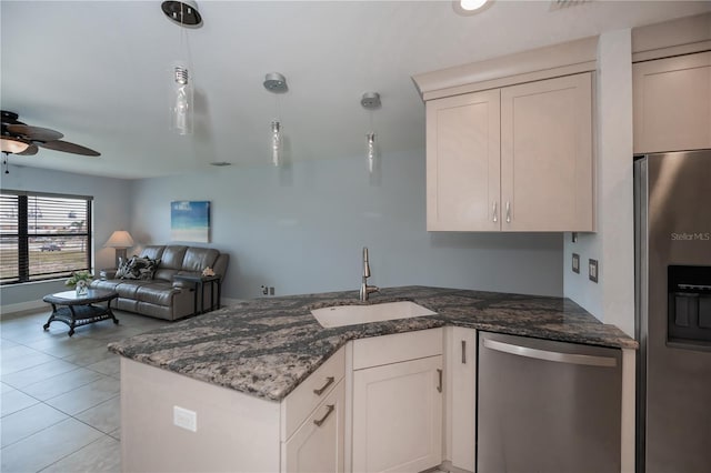 kitchen with stainless steel appliances, open floor plan, a sink, dark stone countertops, and a peninsula