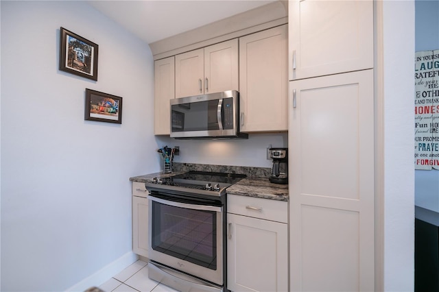 kitchen featuring dark stone countertops, stainless steel appliances, light tile patterned flooring, and baseboards