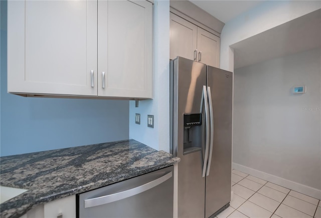 kitchen with light tile patterned floors, appliances with stainless steel finishes, white cabinets, dark stone countertops, and baseboards