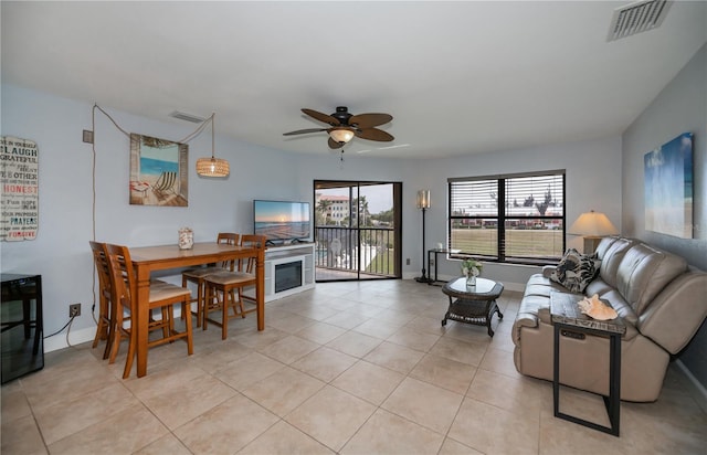 living room featuring ceiling fan, light tile patterned flooring, visible vents, baseboards, and a glass covered fireplace