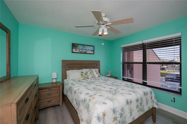 bedroom featuring ceiling fan, a textured ceiling, baseboards, and wood finished floors