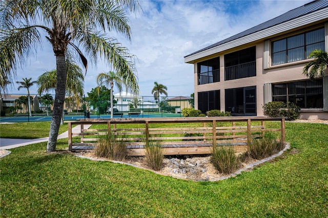 view of property's community with a tennis court, fence, and a lawn