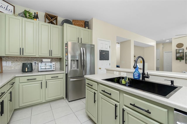 kitchen with a sink, green cabinets, light countertops, stainless steel refrigerator with ice dispenser, and backsplash