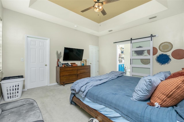 carpeted bedroom featuring a barn door, visible vents, a tray ceiling, and a ceiling fan