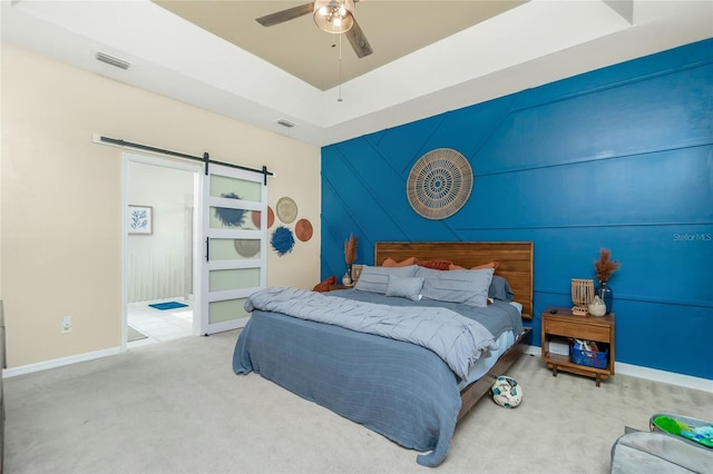 carpeted bedroom with a barn door, a raised ceiling, visible vents, and baseboards