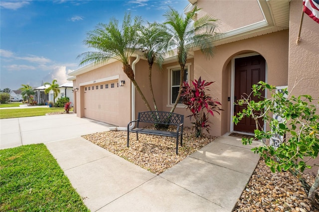 entrance to property with a garage, concrete driveway, and stucco siding