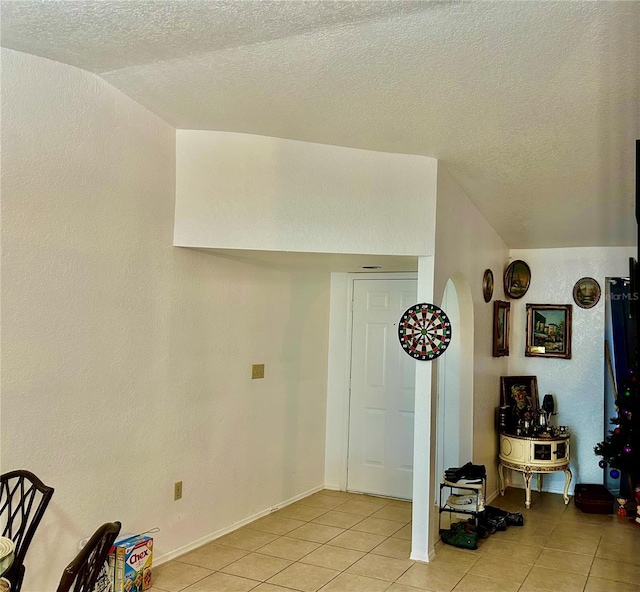 foyer featuring a textured wall, vaulted ceiling, a textured ceiling, and light tile patterned floors