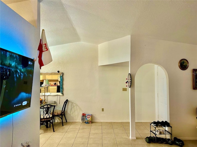 interior space with baseboards, arched walkways, tile patterned flooring, vaulted ceiling, and a textured ceiling