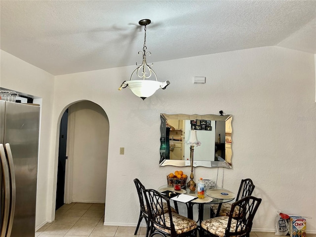 dining space with arched walkways, a textured ceiling, light tile patterned flooring, and lofted ceiling