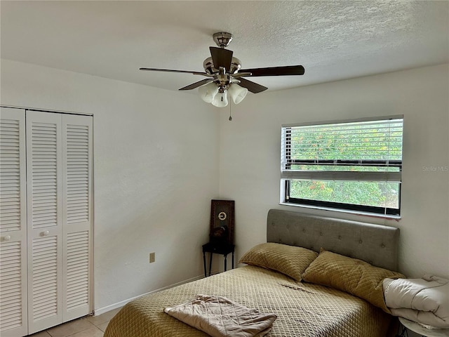 bedroom featuring light tile patterned floors, a textured ceiling, a ceiling fan, baseboards, and a closet