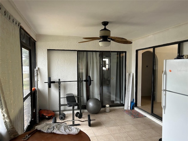 workout area featuring a textured wall, tile patterned flooring, and a ceiling fan