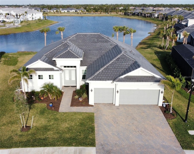 view of front facade featuring a garage, a water view, decorative driveway, a residential view, and stucco siding