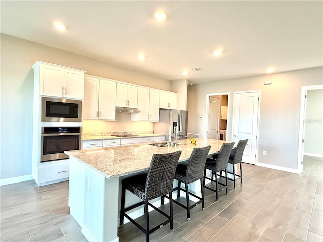 kitchen with stainless steel appliances, white cabinets, a sink, and a large island