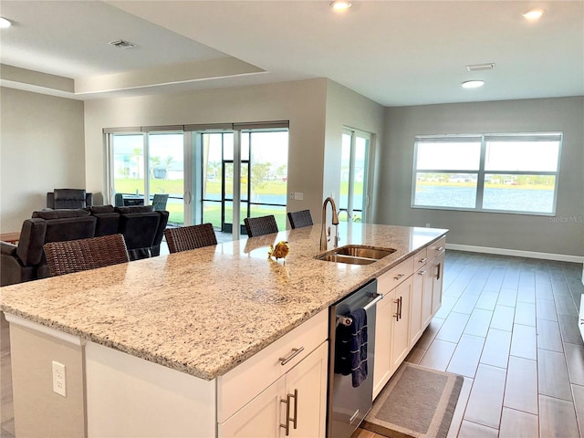 kitchen featuring a center island with sink, dishwasher, open floor plan, light stone countertops, and a sink