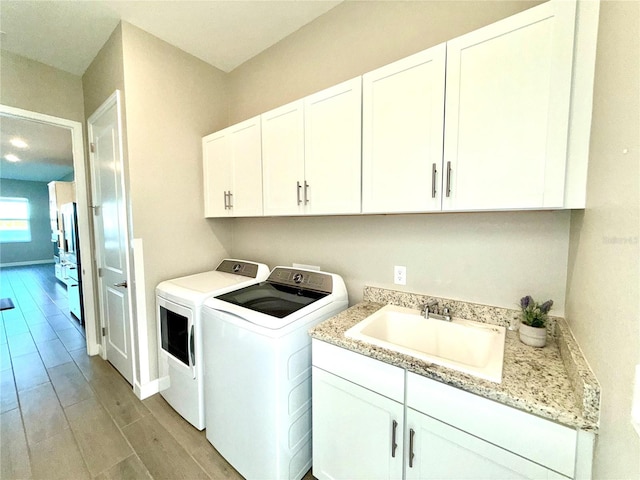 laundry room featuring light wood finished floors, cabinet space, a sink, independent washer and dryer, and baseboards