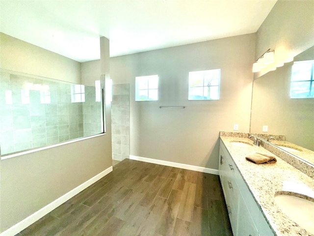 full bathroom featuring double vanity, baseboards, wood finished floors, walk in shower, and a sink